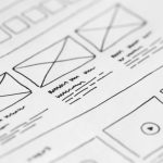 Close-up view of a wireframe design sketch on paper, showcasing layout structures and placeholder elements for a website.