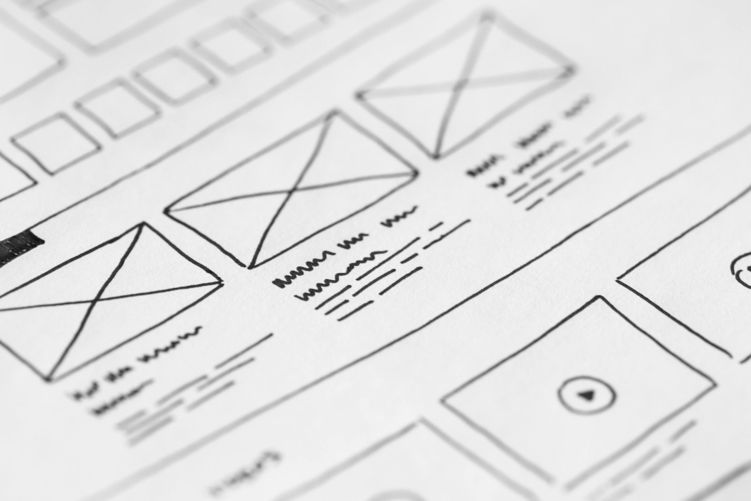 Close-up view of a wireframe design sketch on paper, showcasing layout structures and placeholder elements for a website.